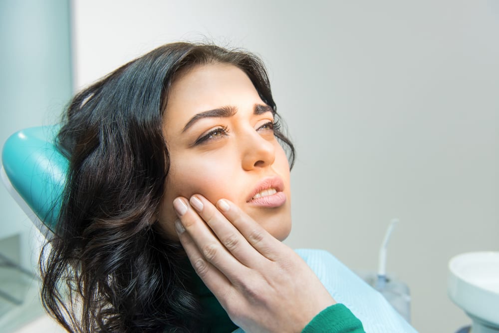 young woman sitting in dental chair with tooth pain